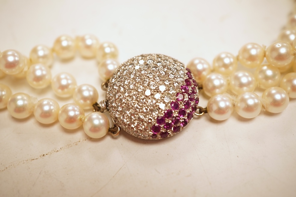 A cultured pearl, ruby and diamond clasp, composed of three rows of cultured pearls measuring approximately 6.9mm diameter, to a white precious metal (tests as 14k) disc-shaped clasp pavé-set with brilliant-cut diamonds